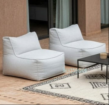 Fauteuils poufs lounge modernes en tissu gris clair, installés sur une terrasse extérieure au bord de la piscine avec table basse noire et tapis berbère décoratif.